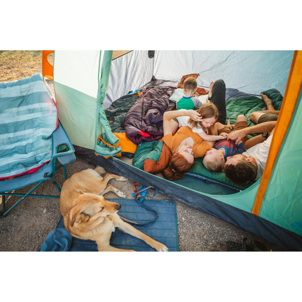 Family camping in tent with sleeping bags, dog resting outside, blue camping chair nearby