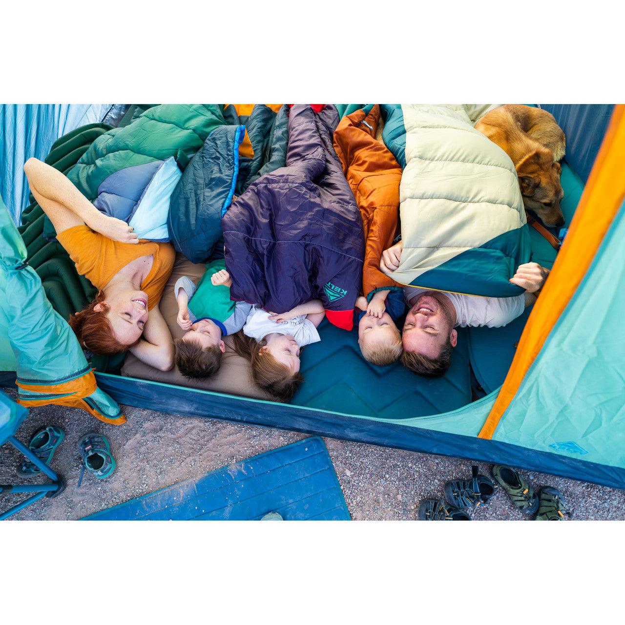 Family with kids and dog camping in a tent, lying in sleeping bags outdoors