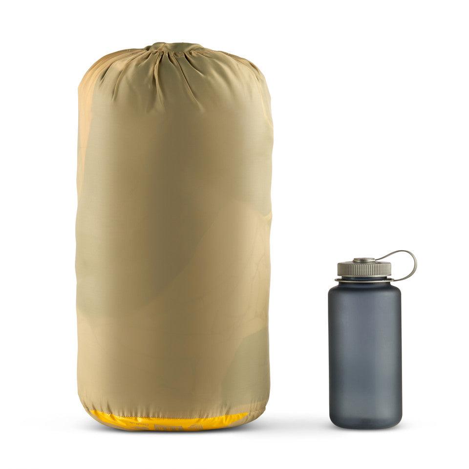Large tan compression sack next to a gray water bottle on white background