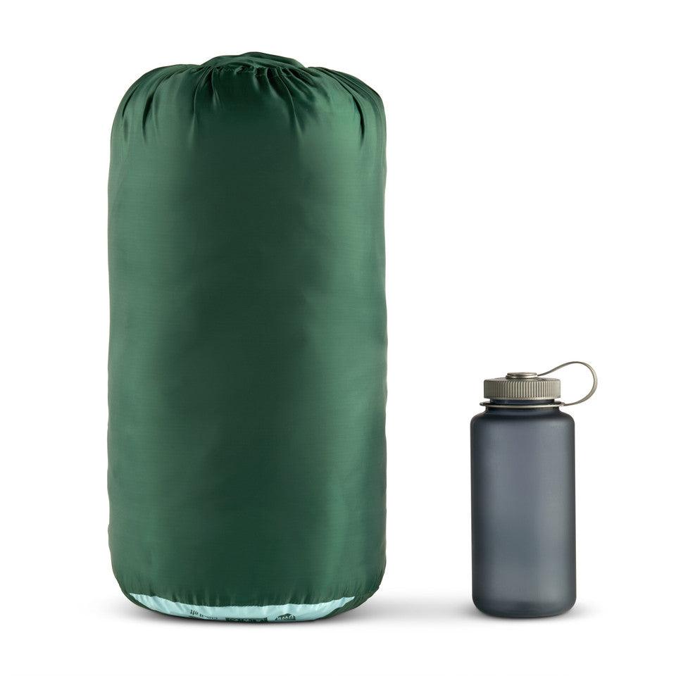 Large green sleeping bag in stuff sack beside gray water bottle on white background