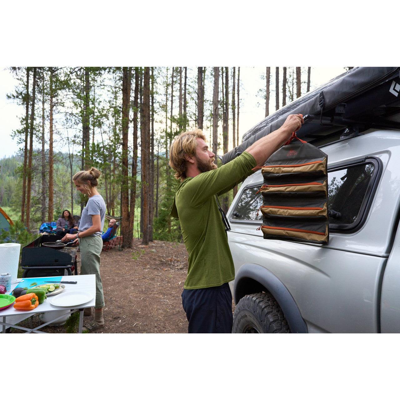 Man hangs Beluga Dull Gold chef roll organizer on truck at campsite with people cooking outdoors