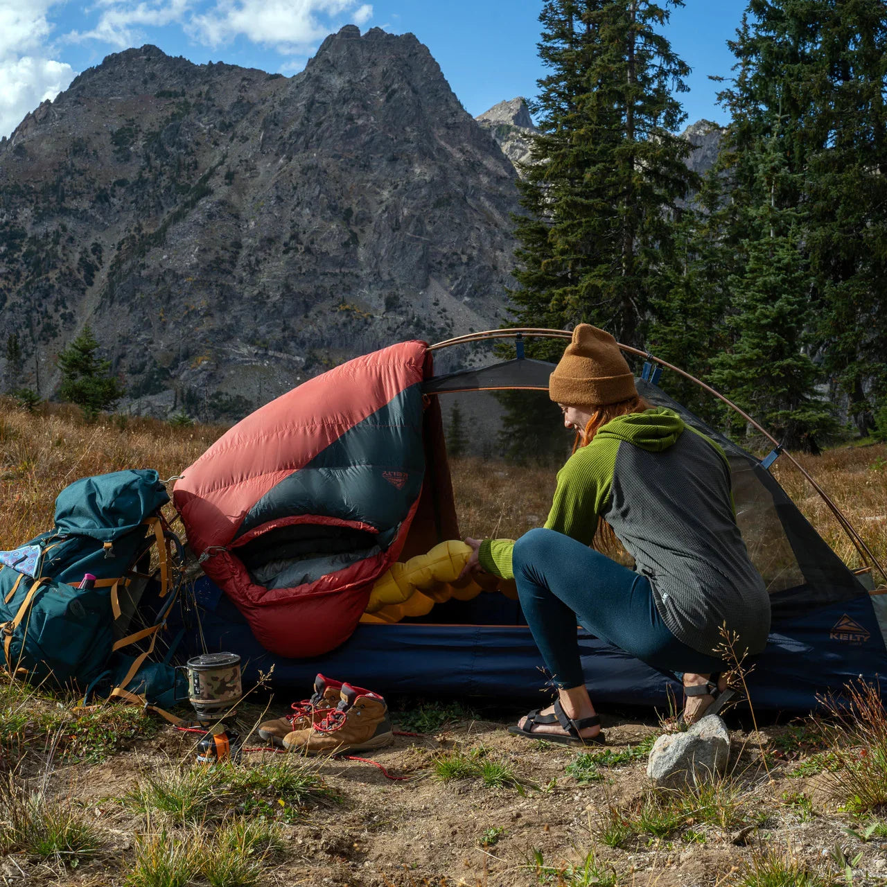 Camper setting up a tent with sleeping bag in mountain wilderness, hiking gear nearby