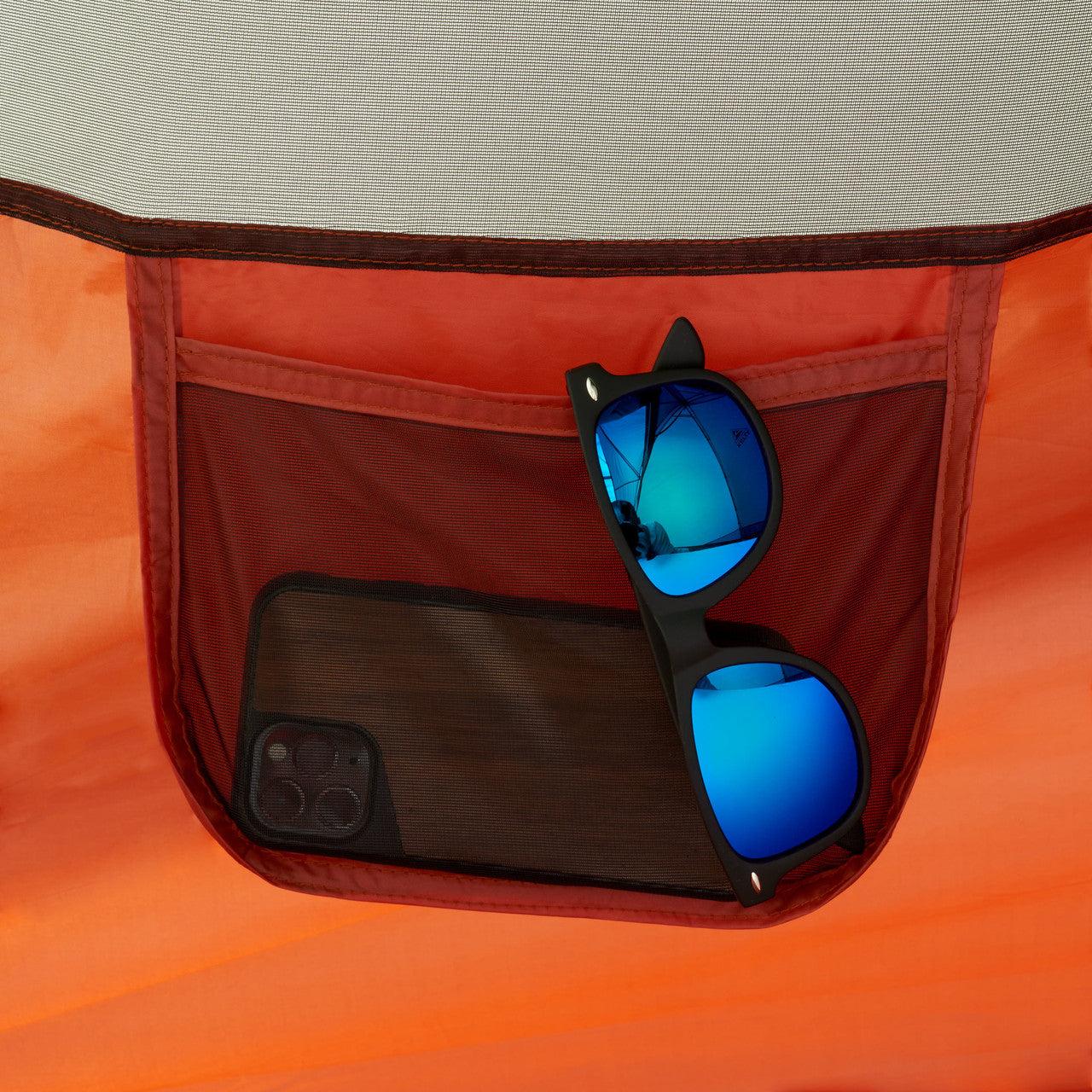 Blue mirrored sunglasses and smartphone in mesh pocket of orange camping tent