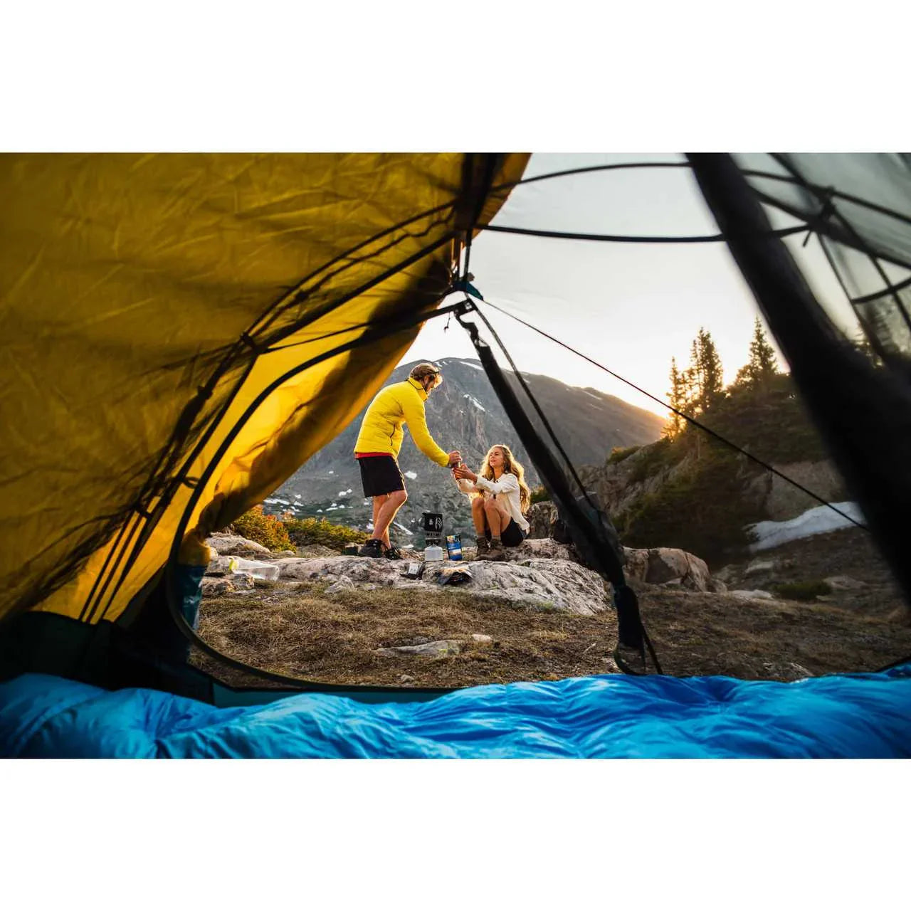 View from inside Kelty Far Out 2 tent, two campers outside in mountain landscape at sunset