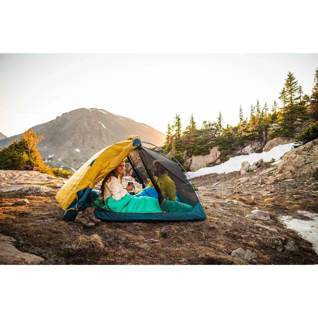 Two people in a Kelty Far Out 2 tent with footprint, camping on rocky terrain at sunrise in the mountains