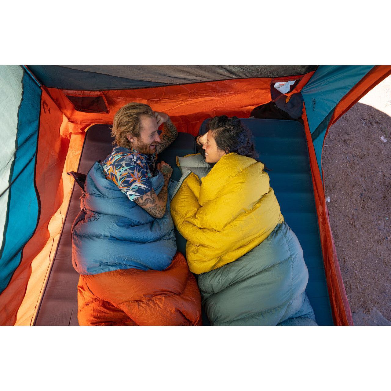 Two people in colorful sleeping bags relaxing inside a tent while camping outdoors.