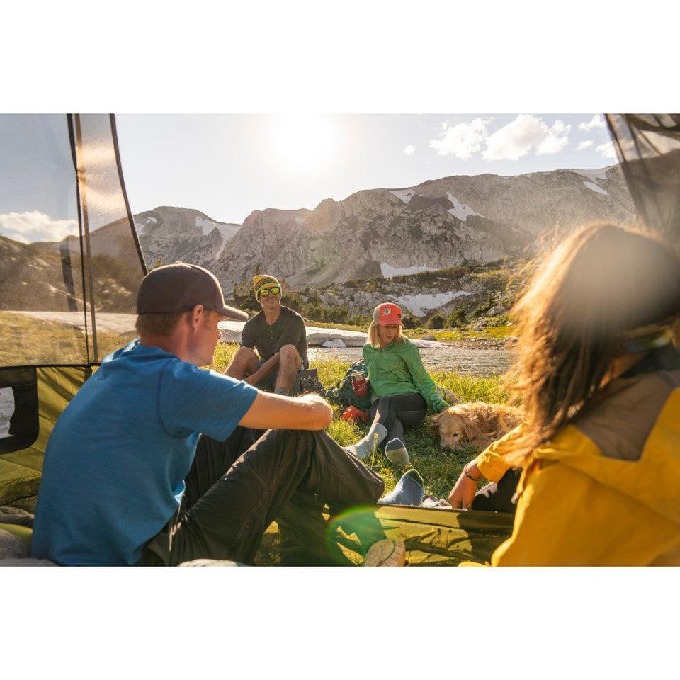 Group of hikers relaxing by a tent in the mountains, enjoying a sunny day outdoors