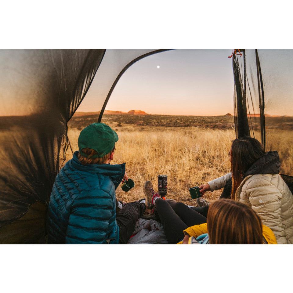 Campers relaxing inside Kelty Grand Mesa 2 tent, looking out over a dry grass landscape at sunset.