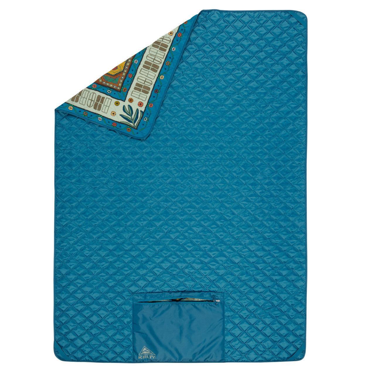 Quilted blue camping blanket with corner folded to show colorful patterned lining and Kelty pocket