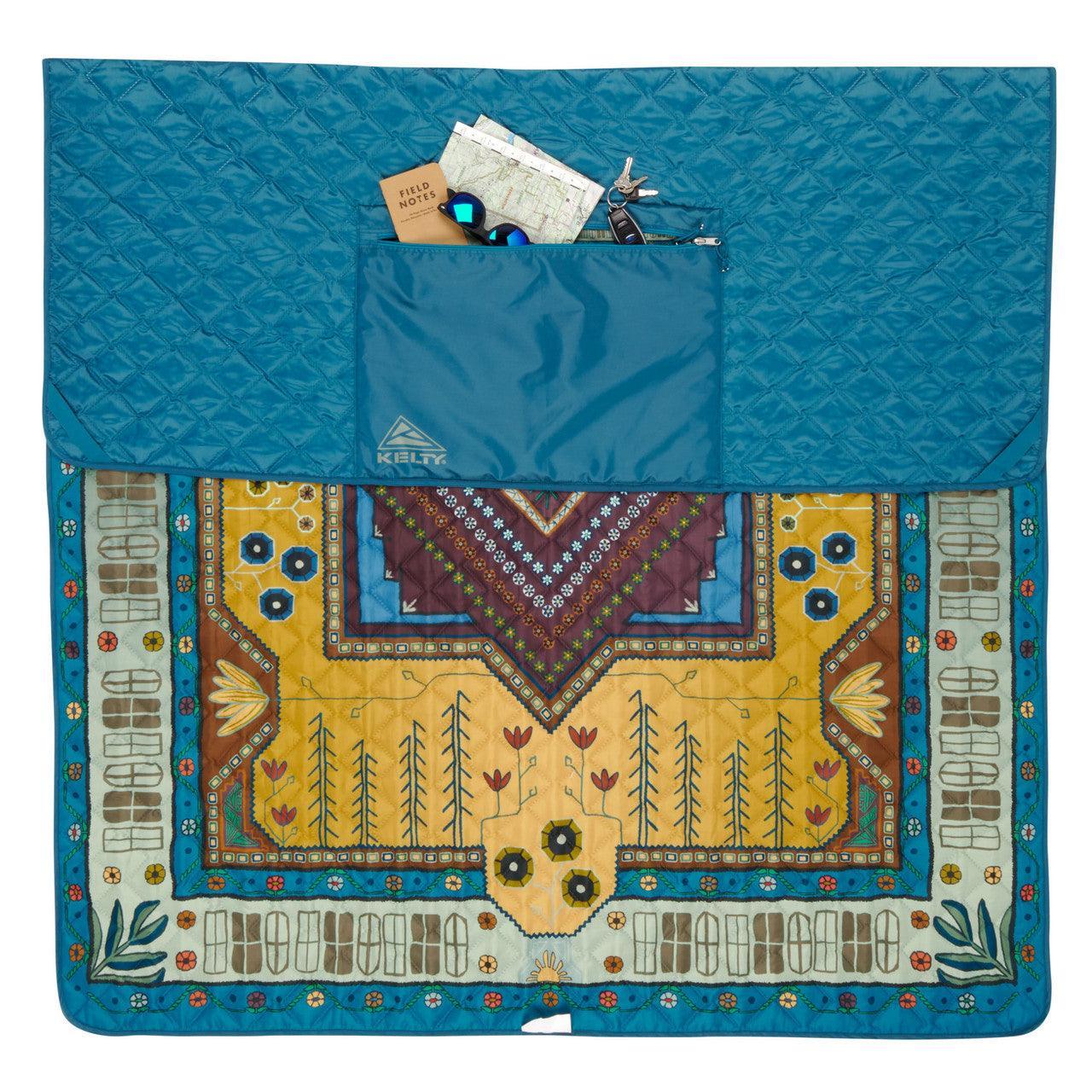 Colonial blue Kelty blanket with floral geometric pattern and pocket holding map, notebook, sunglasses, and keys