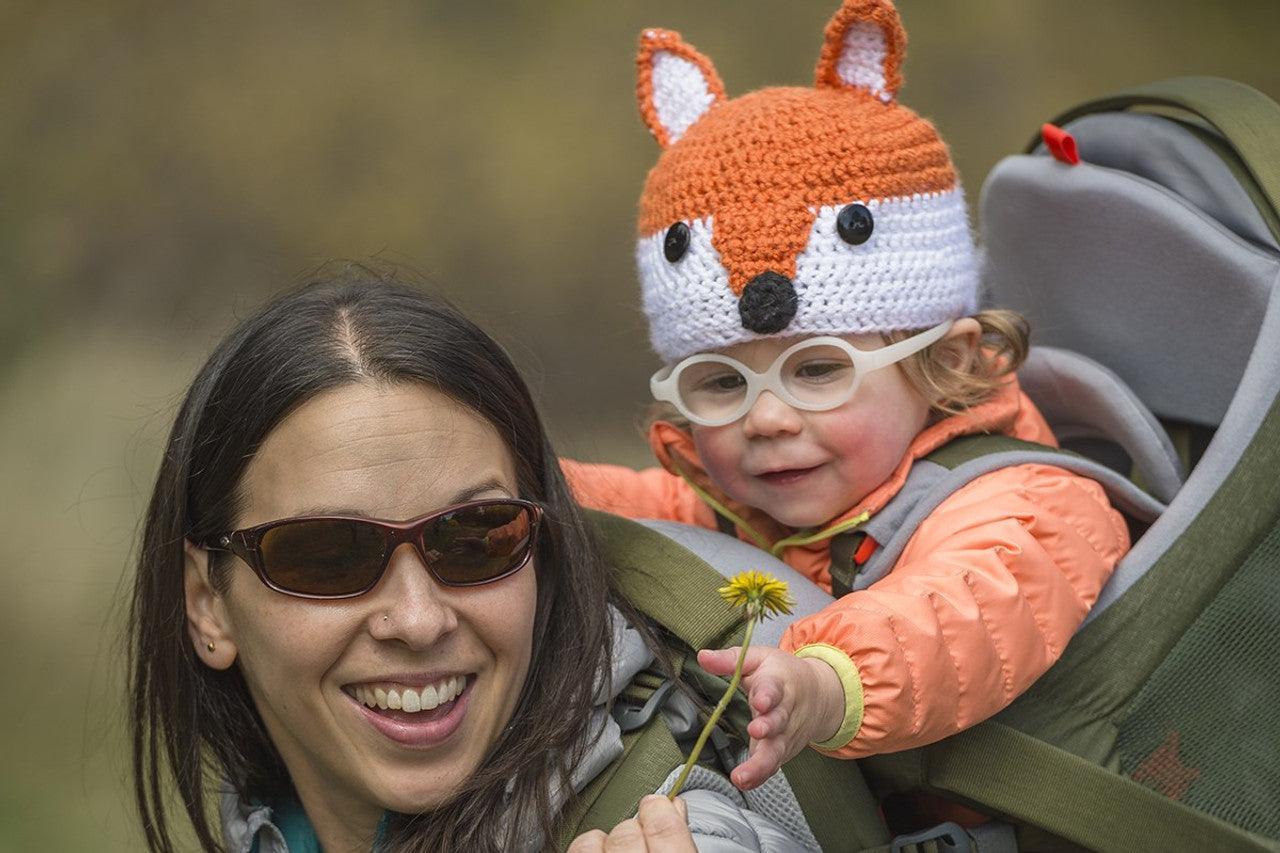 Woman hiking with toddler in child carrier, toddler wearing fox hat and glasses outdoors