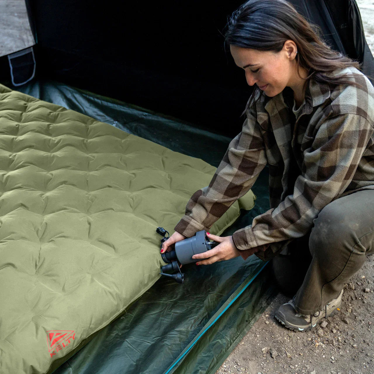 Woman inflating green camping air mattress inside tent outdoors