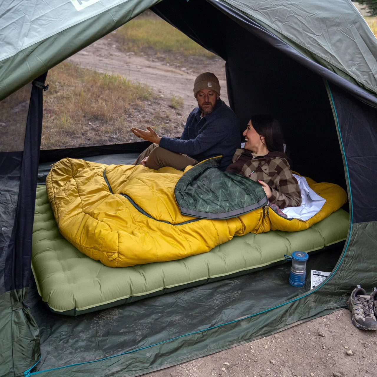 Couple camping in a tent with yellow sleeping bag on green air mattress outdoors
