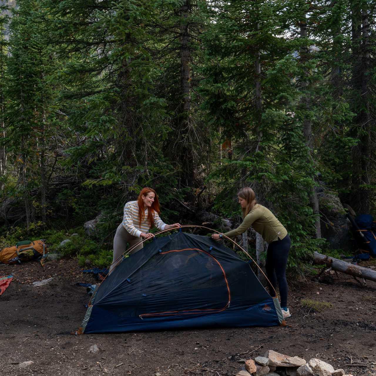 Two women setting up a Kelty Late Start 2P Tent in a forest campsite