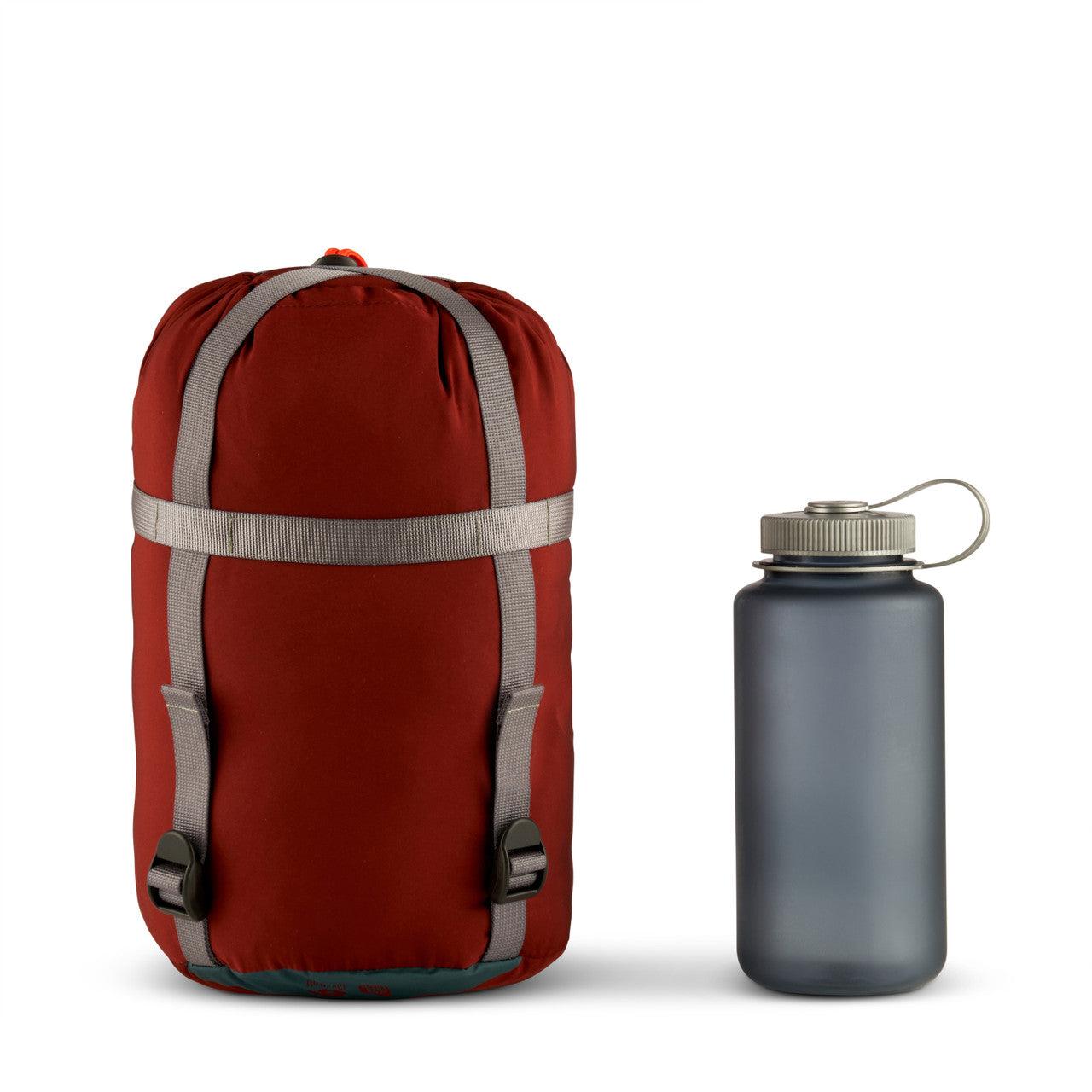 Red compression sack with gray straps next to a matte gray water bottle on white background