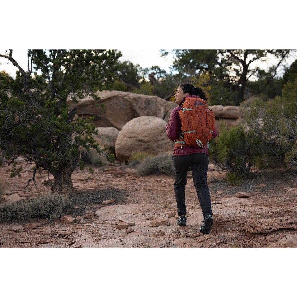 Woman hiking on rocky trail with orange Kelty Redwing 36 backpack in desert landscape