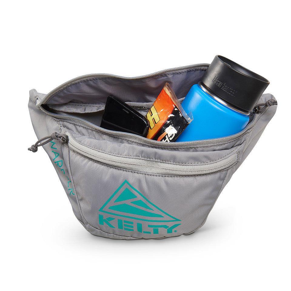 Kelty Warbler fanny pack in gray with blue water bottle, snack bar, and phone inside.