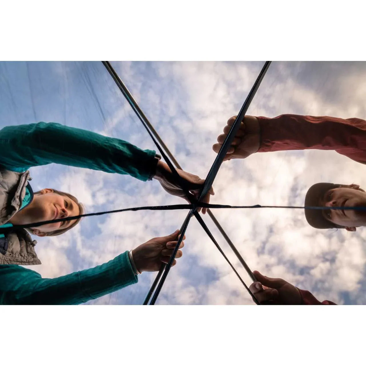 Campers assembling Kelty Wireless 2 tent poles under a cloudy sky outdoors