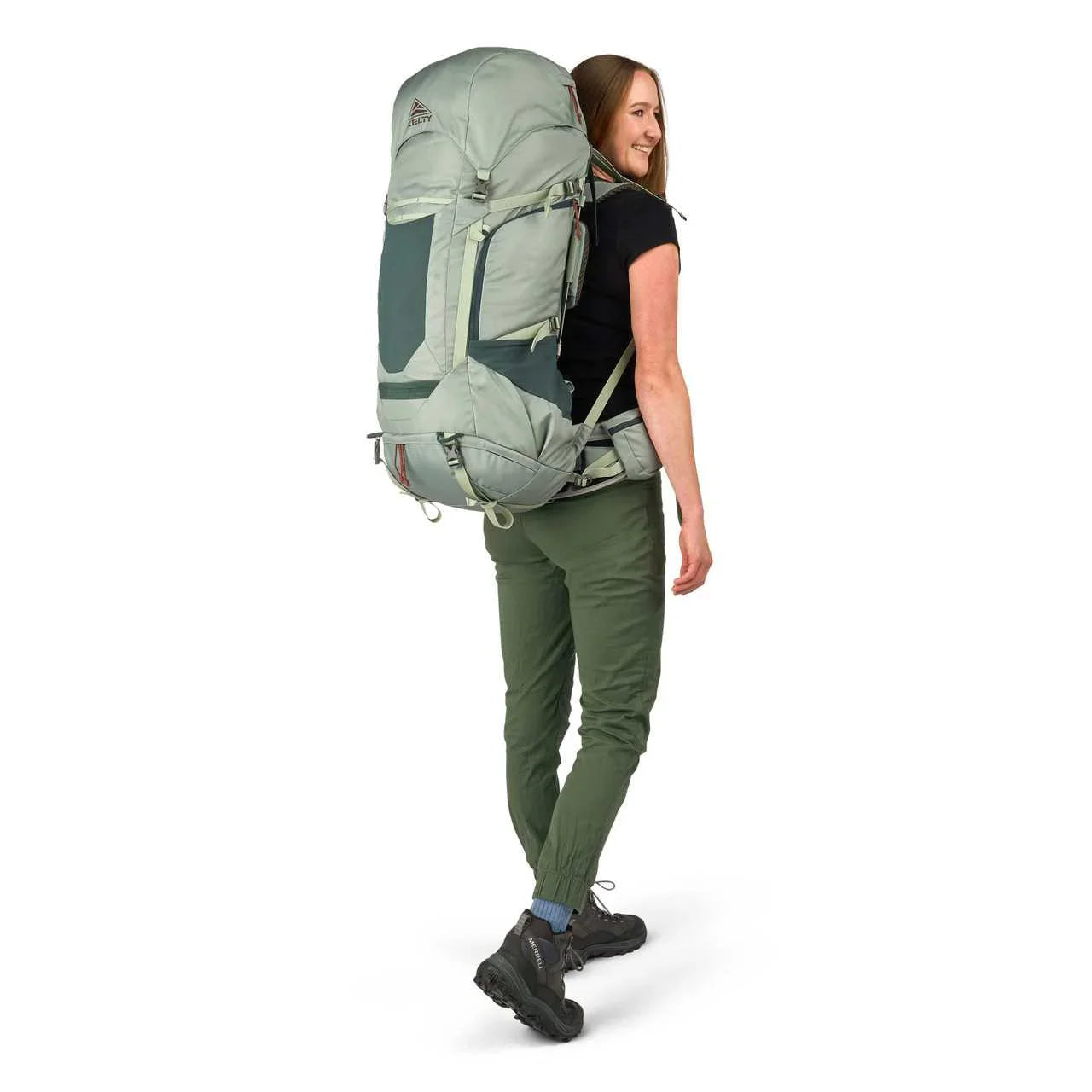 Woman wearing Kelty Glendale 65L backpack in green, standing against white background
