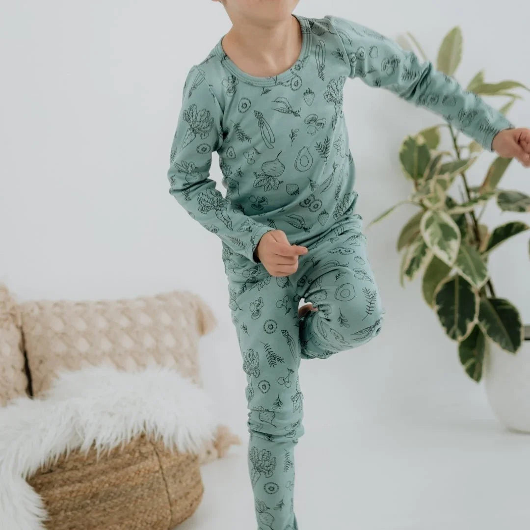 Child in green bamboo lounge set with veggie print, standing indoors by a plant