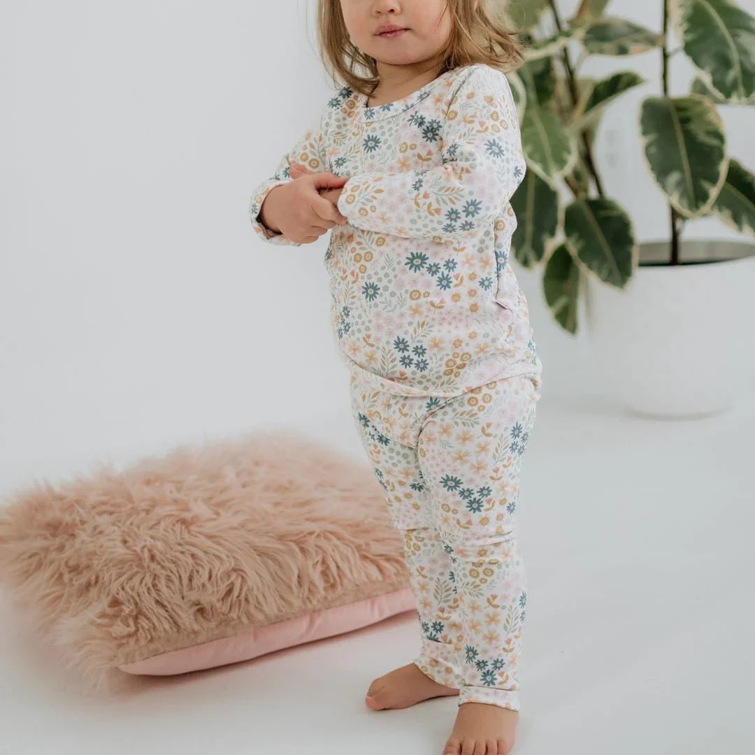 Toddler in floral bamboo lounge set poses indoors with pink fuzzy pillow and potted plant
