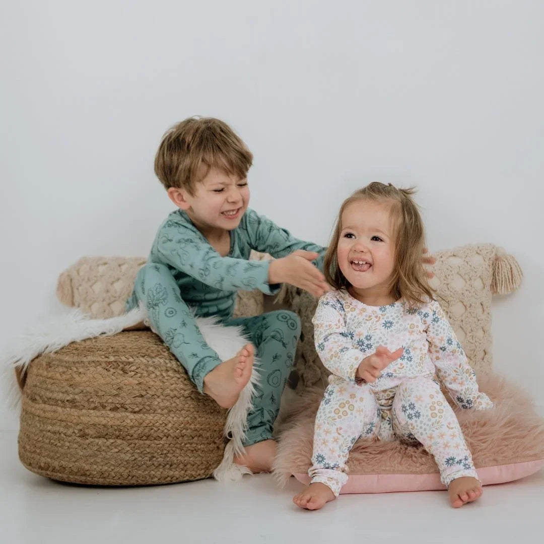 Two kids in bamboo lounge sets sitting on cozy pillows, smiling in a bright room