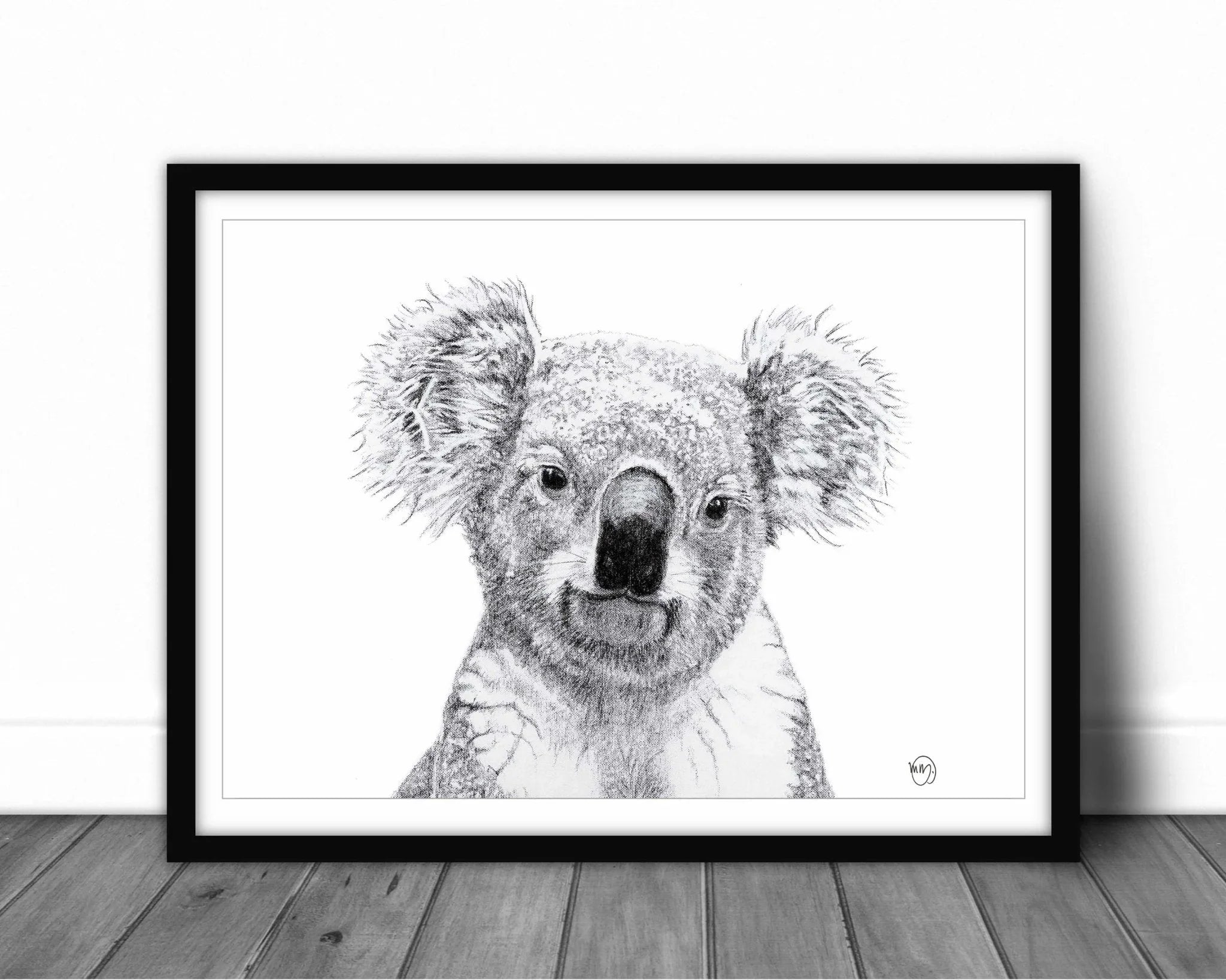 Framed black and white koala portrait drawing on wooden floor against white wall