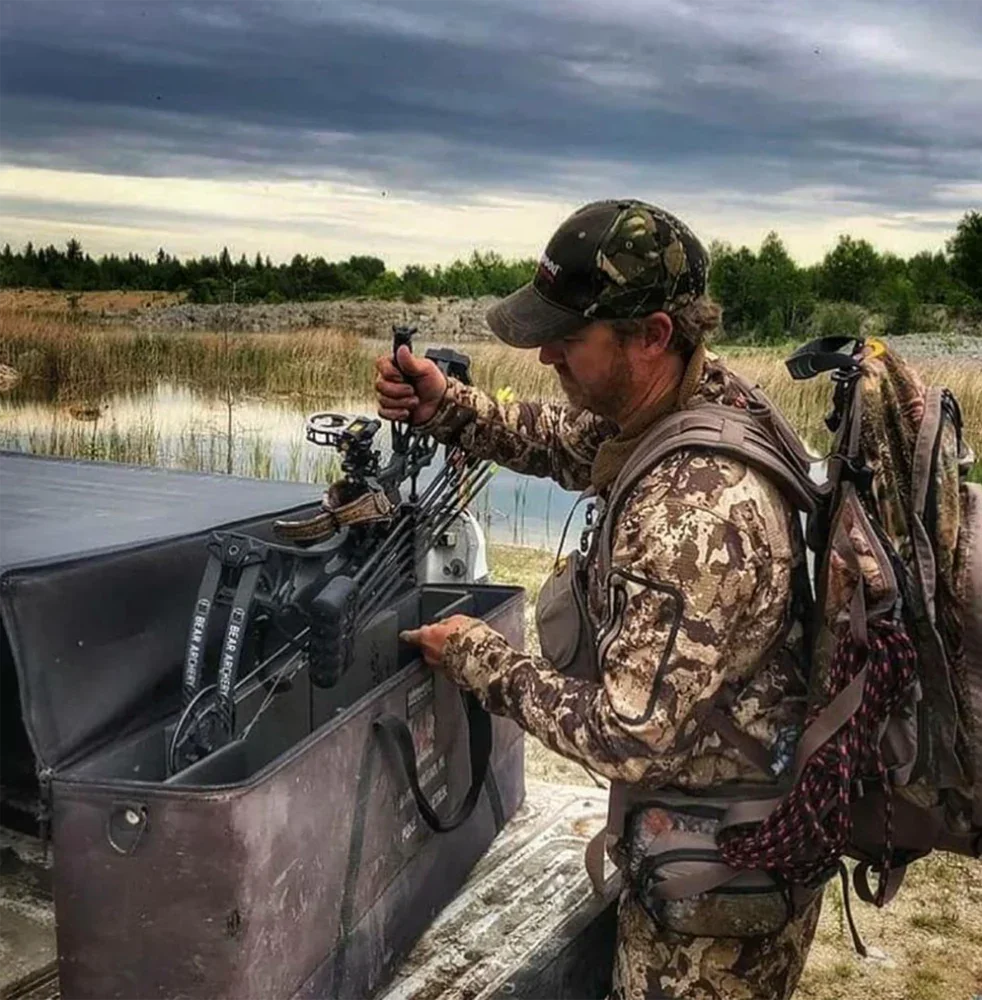 Hunter in camouflage gear loading compound bow from case outdoors near marshland