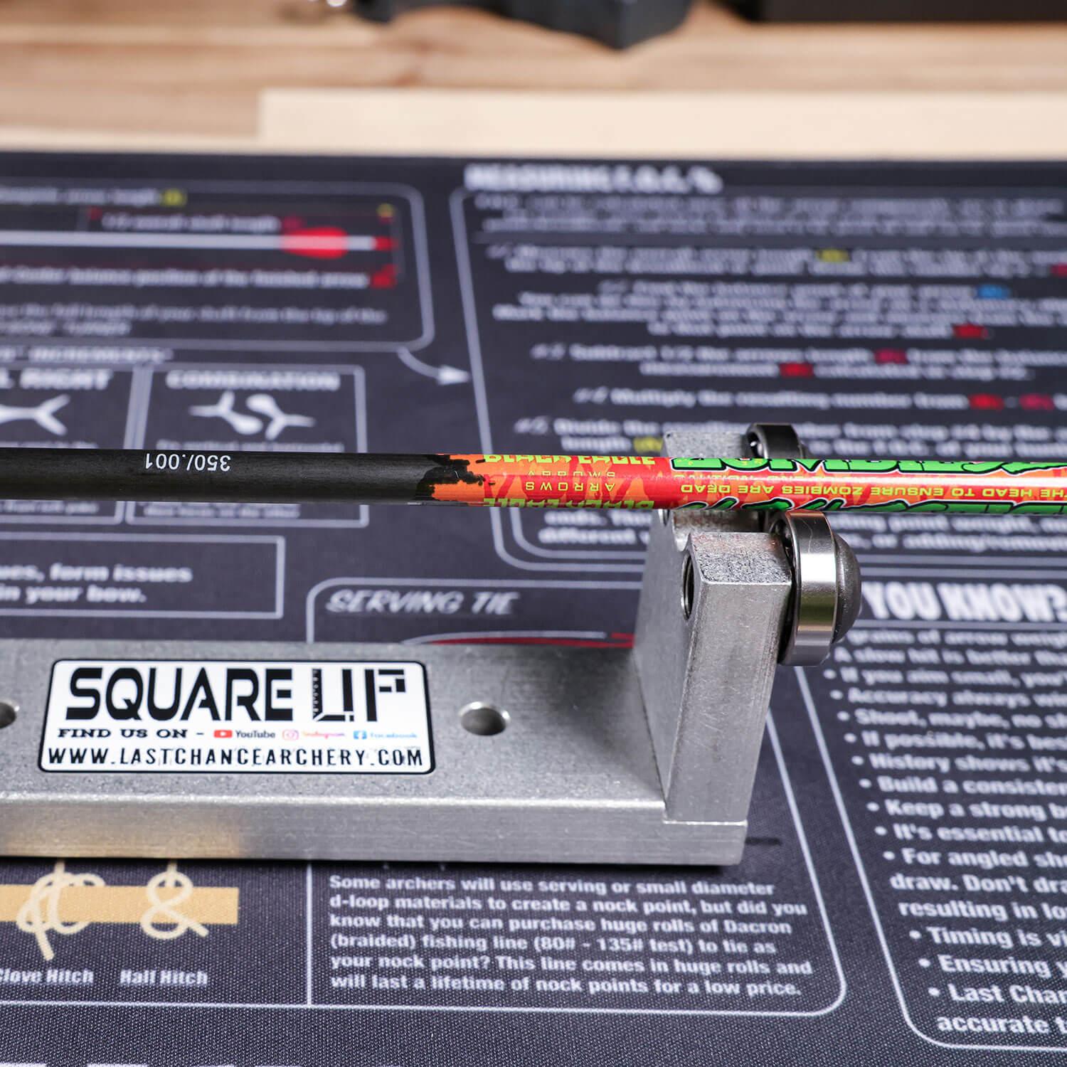 Archery squaring tool SQUARE UP aligning an arrow on a mat with instructional text.