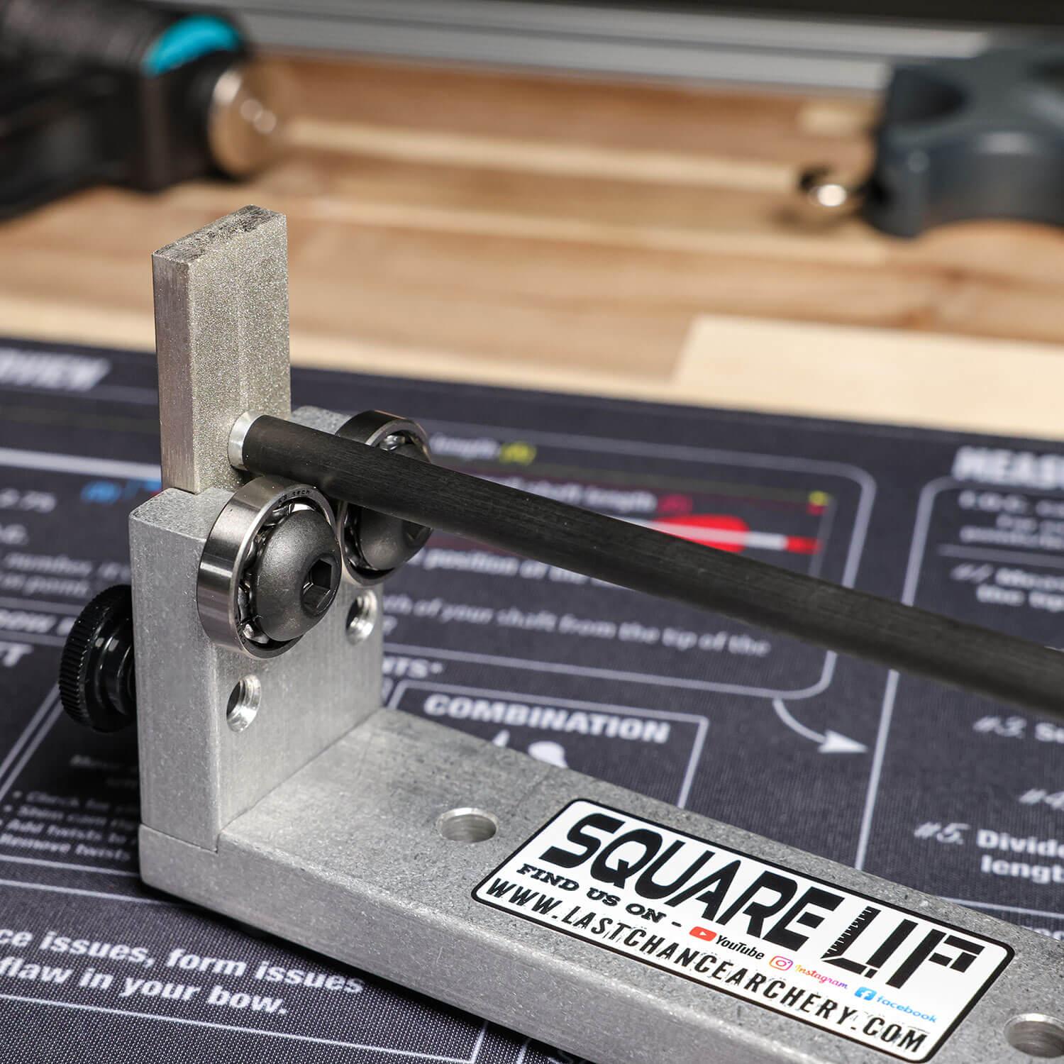 Archery arrow squaring tool on workbench with arrow shaft, Last Chance Archery branding visible.