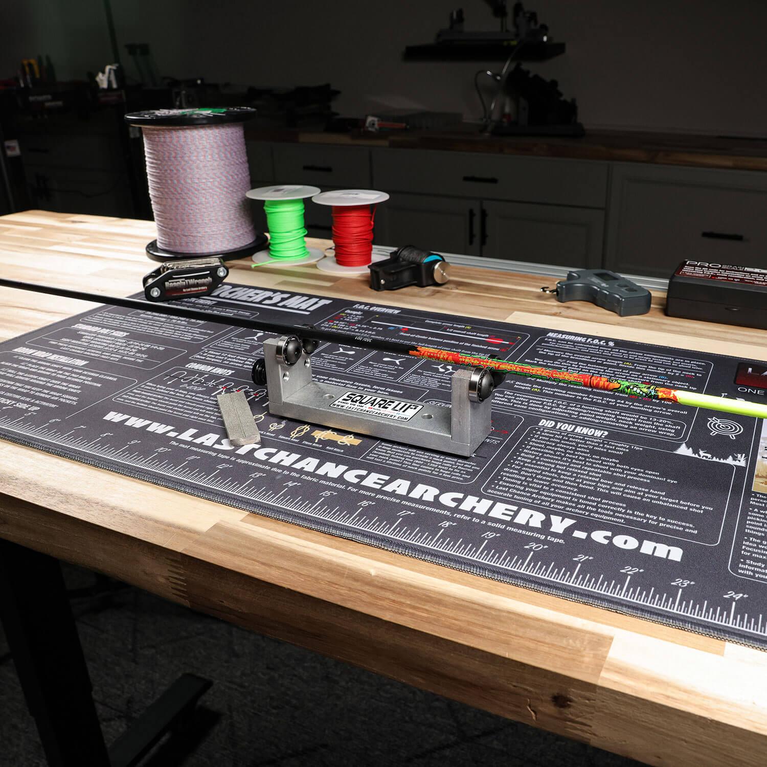 Archery squaring tool with arrow on a workbench, string spools and tools in background