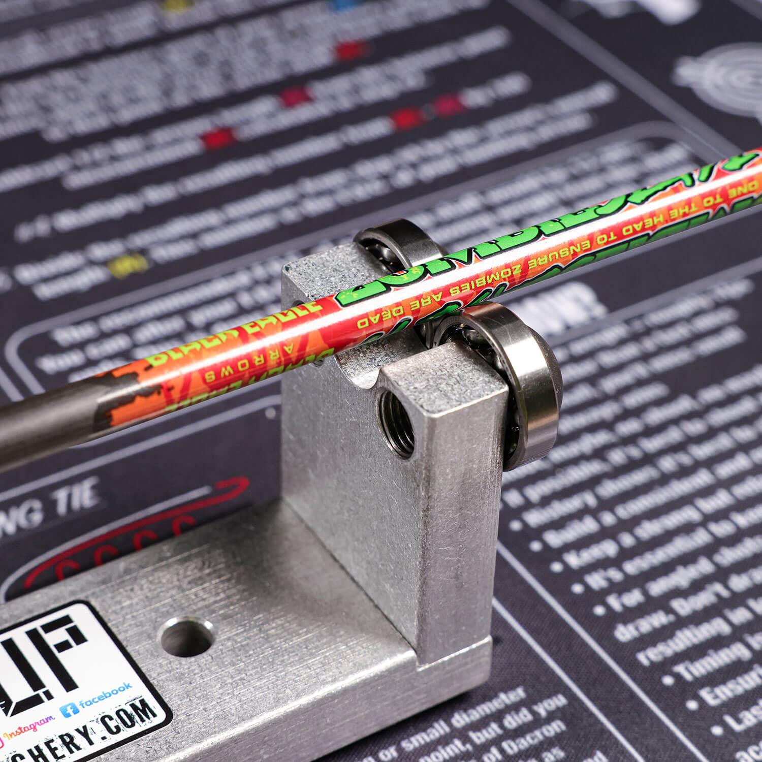 Archery arrow squaring tool aligning a colorful arrow shaft on a printed instruction mat