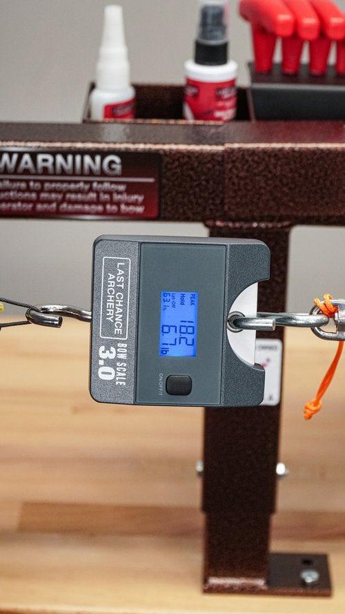 Last Chance Archery Bow Scale 3.0 measuring draw weight on a bow in a workshop setting