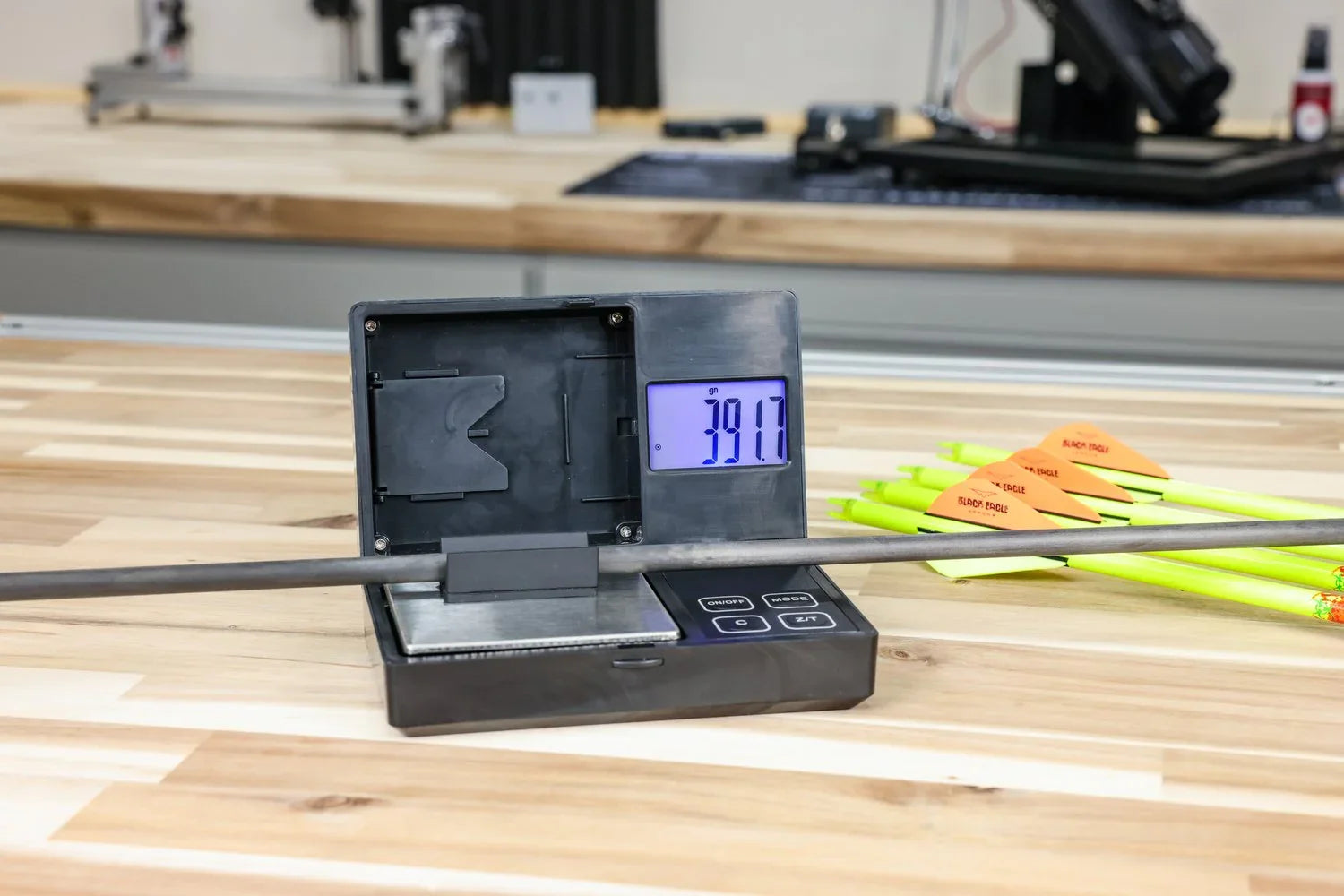 Arrow shaft weighed on digital scale, yellow fletched arrows on wooden workbench