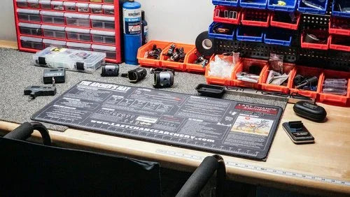 Archery workbench with The Archers Mat, tools, camera gear, and organized storage bins