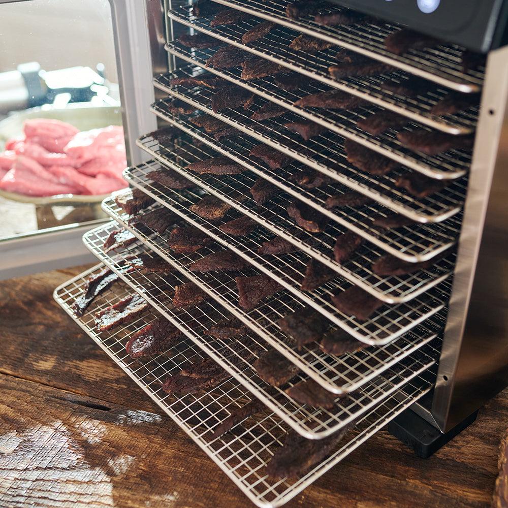 10-tray stainless steel food dehydrator with racks of beef jerky in kitchen setting.
