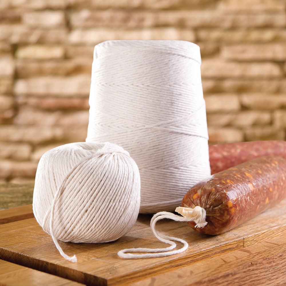 Cotton twine spools and tied sausage on wooden board, kitchen background