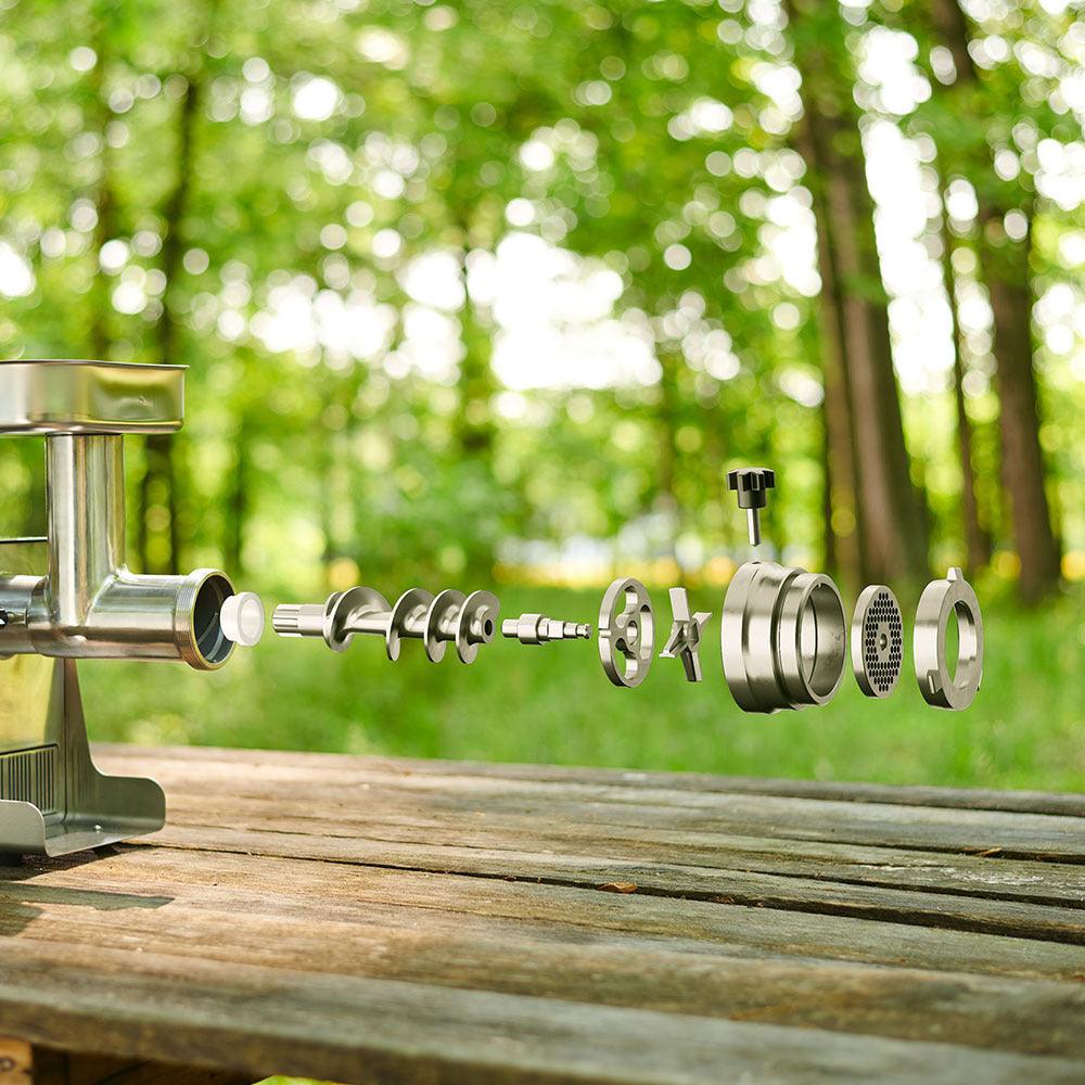 Stainless steel meat grinder adapter parts exploded on a wooden table outdoors