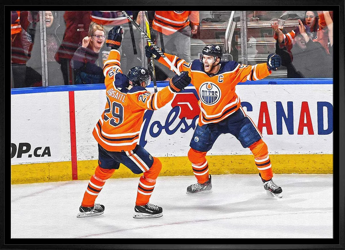Two Edmonton Oilers hockey players celebrate a goal on ice with cheering fans in the background.