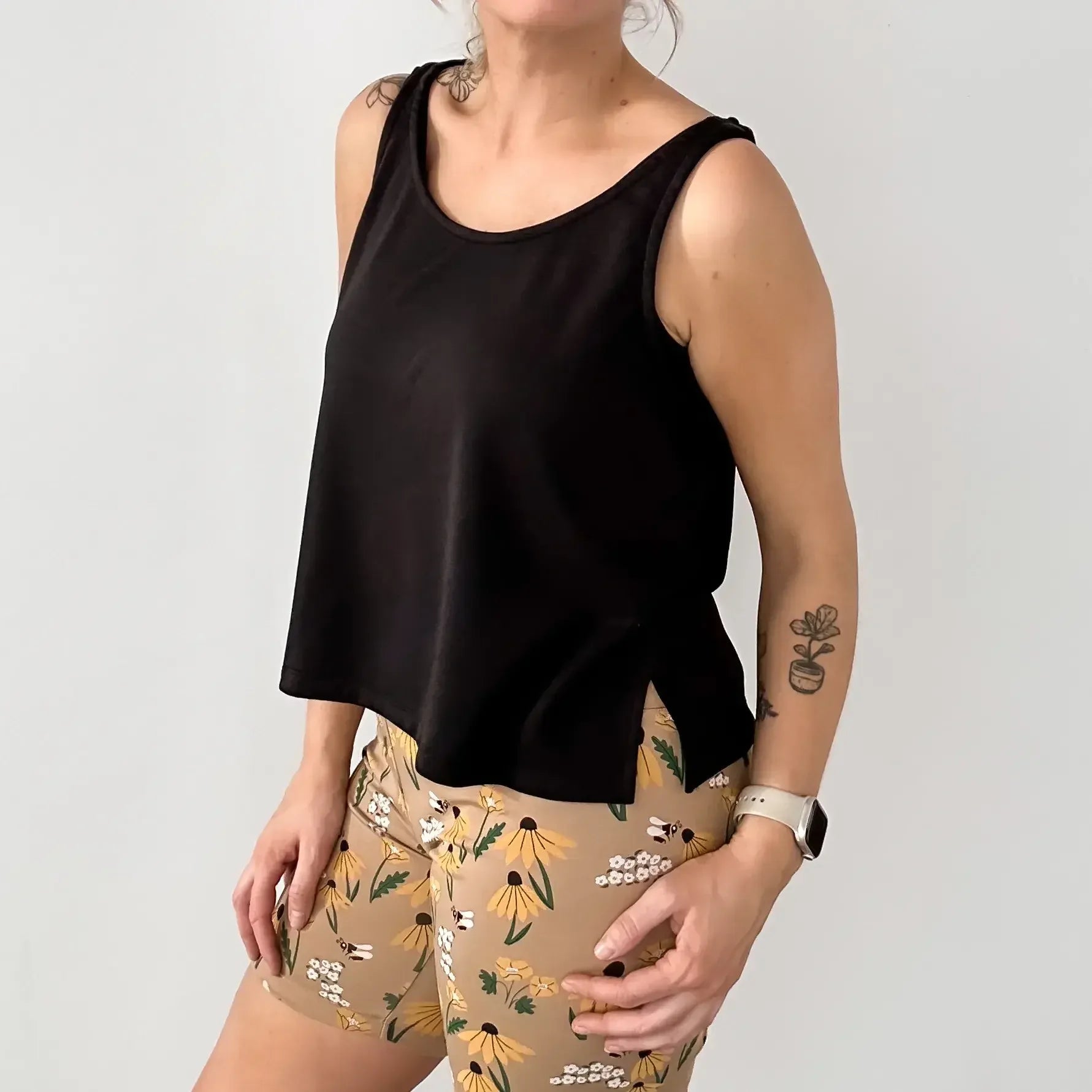Woman in black sleeveless tank top and beige floral shorts with tattoos and smartwatch