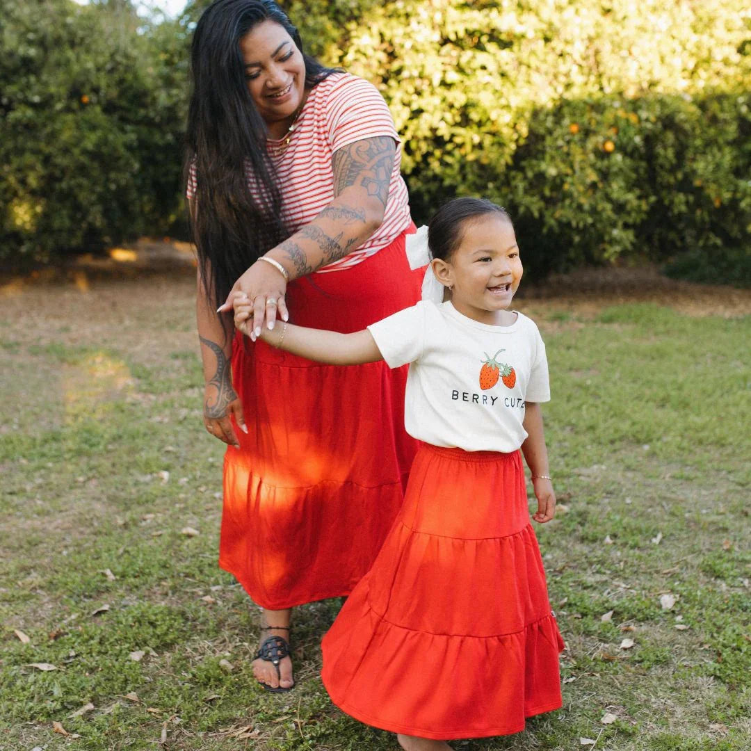 Woman and child in matching red skirts smiling in a sunny garden, family outdoor fashion