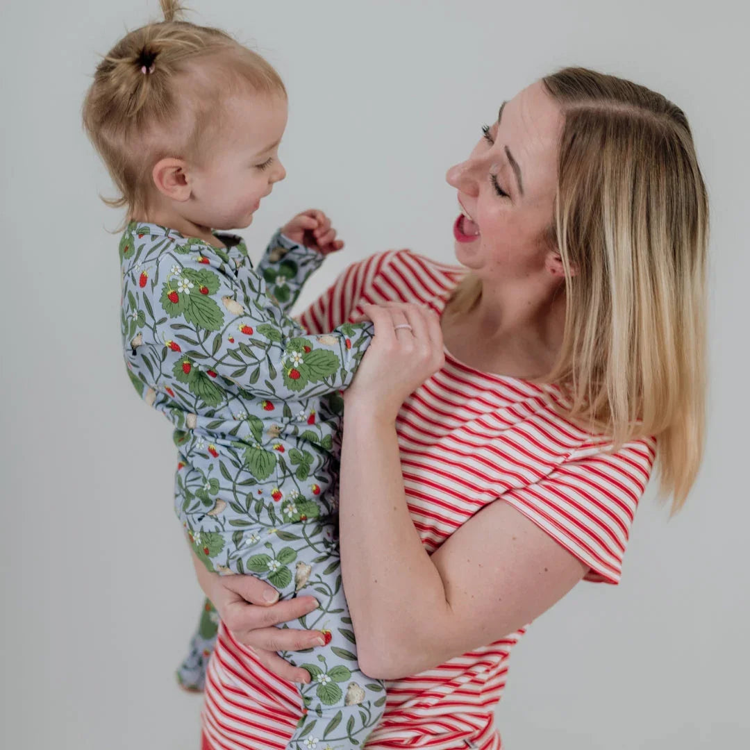 Smiling mom in red striped shirt holding baby in floral pajama, light background