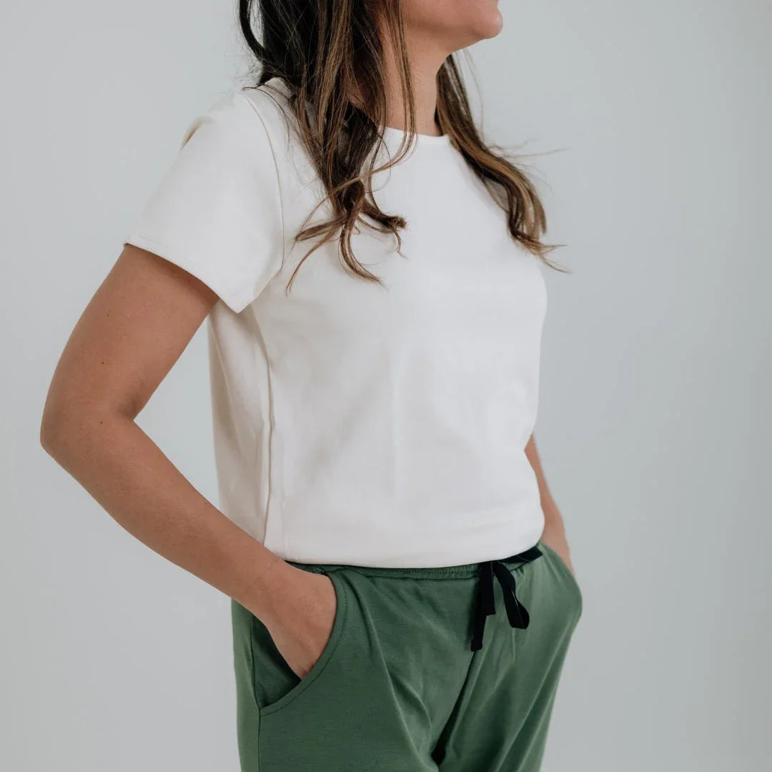 Woman in a white short-sleeve t-shirt and green drawstring pants with hands in pockets