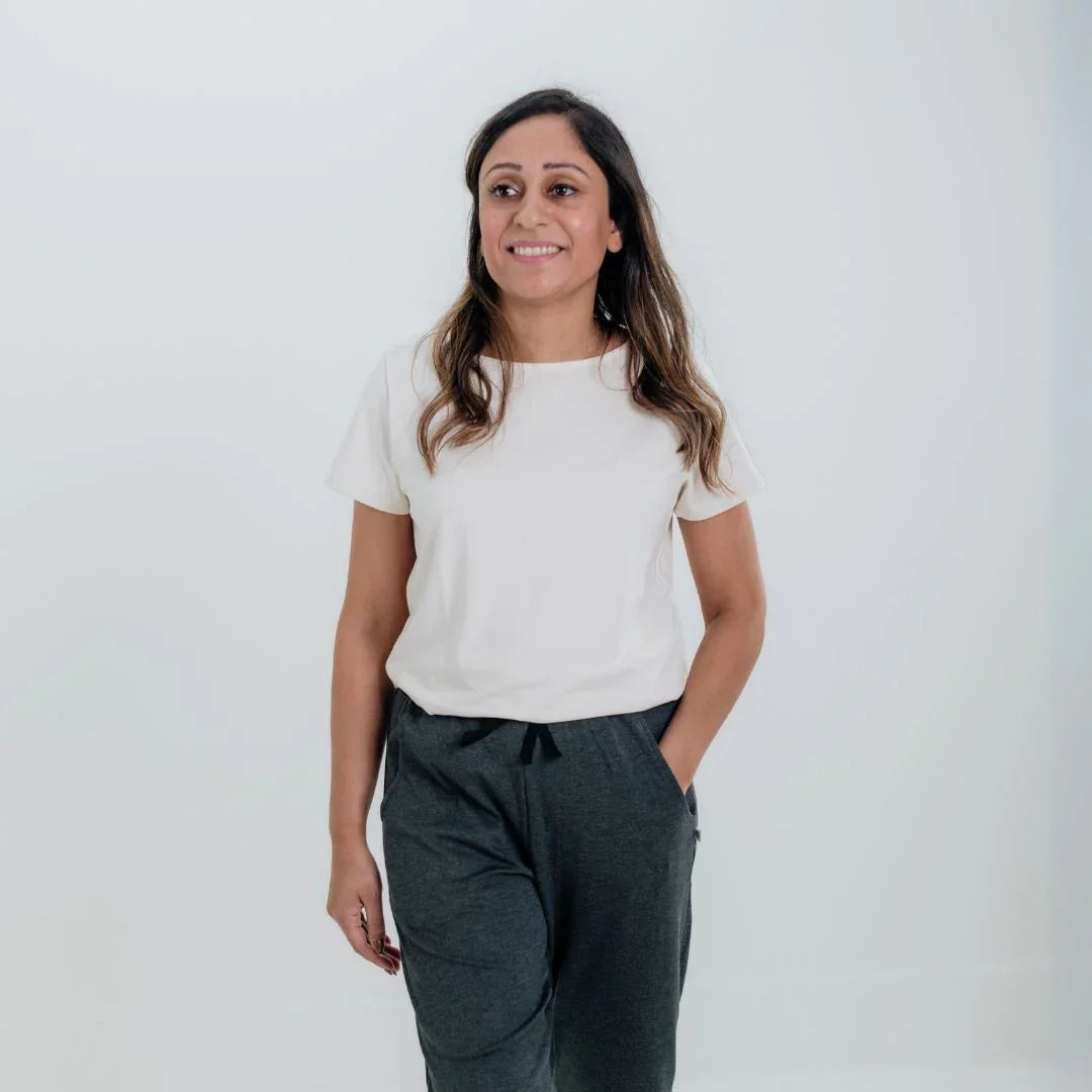 Woman in casual white t-shirt and gray joggers standing against a plain white background