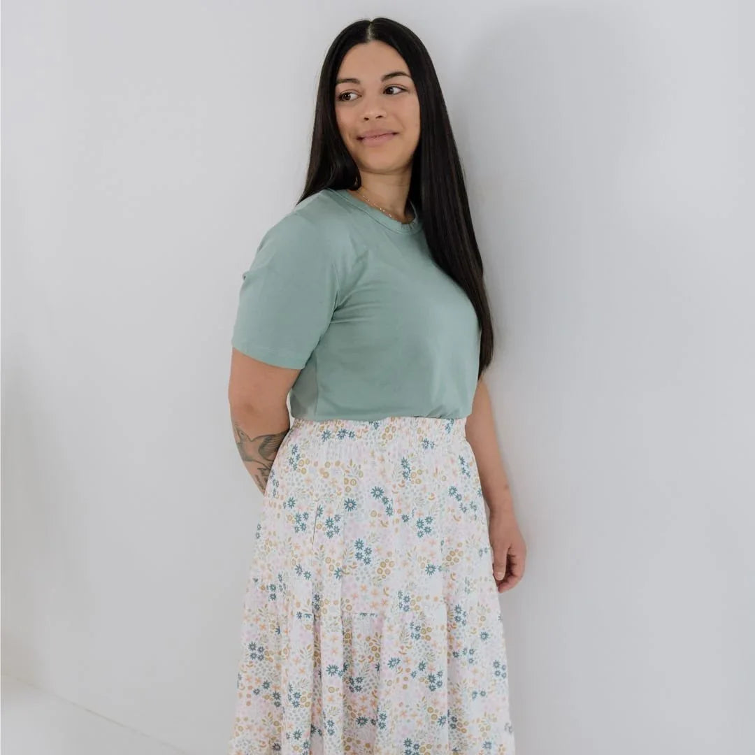 Woman in light green bamboo t-shirt and floral skirt standing against white wall
