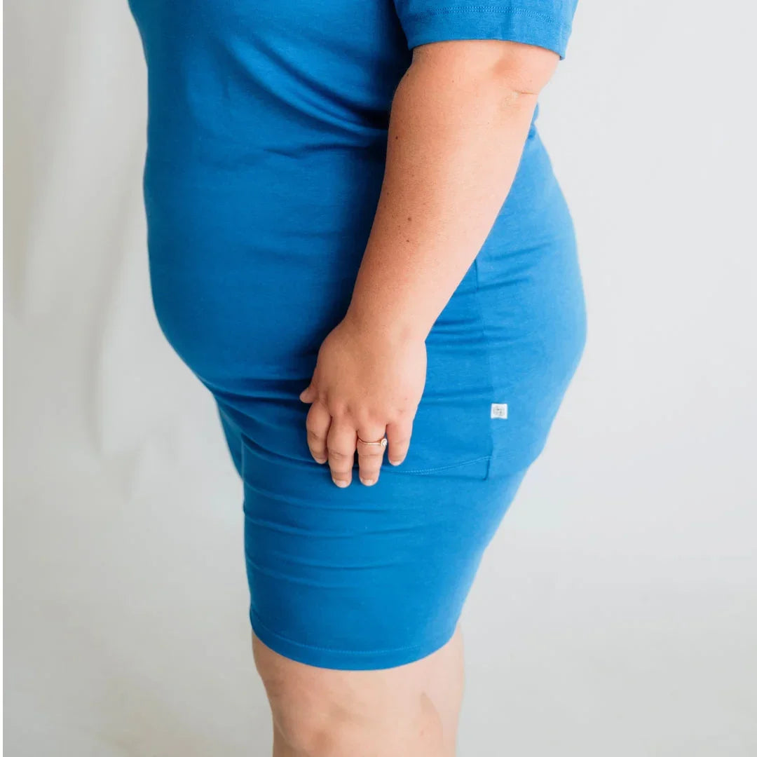 Plus size woman in blue fitted dress standing against light background
