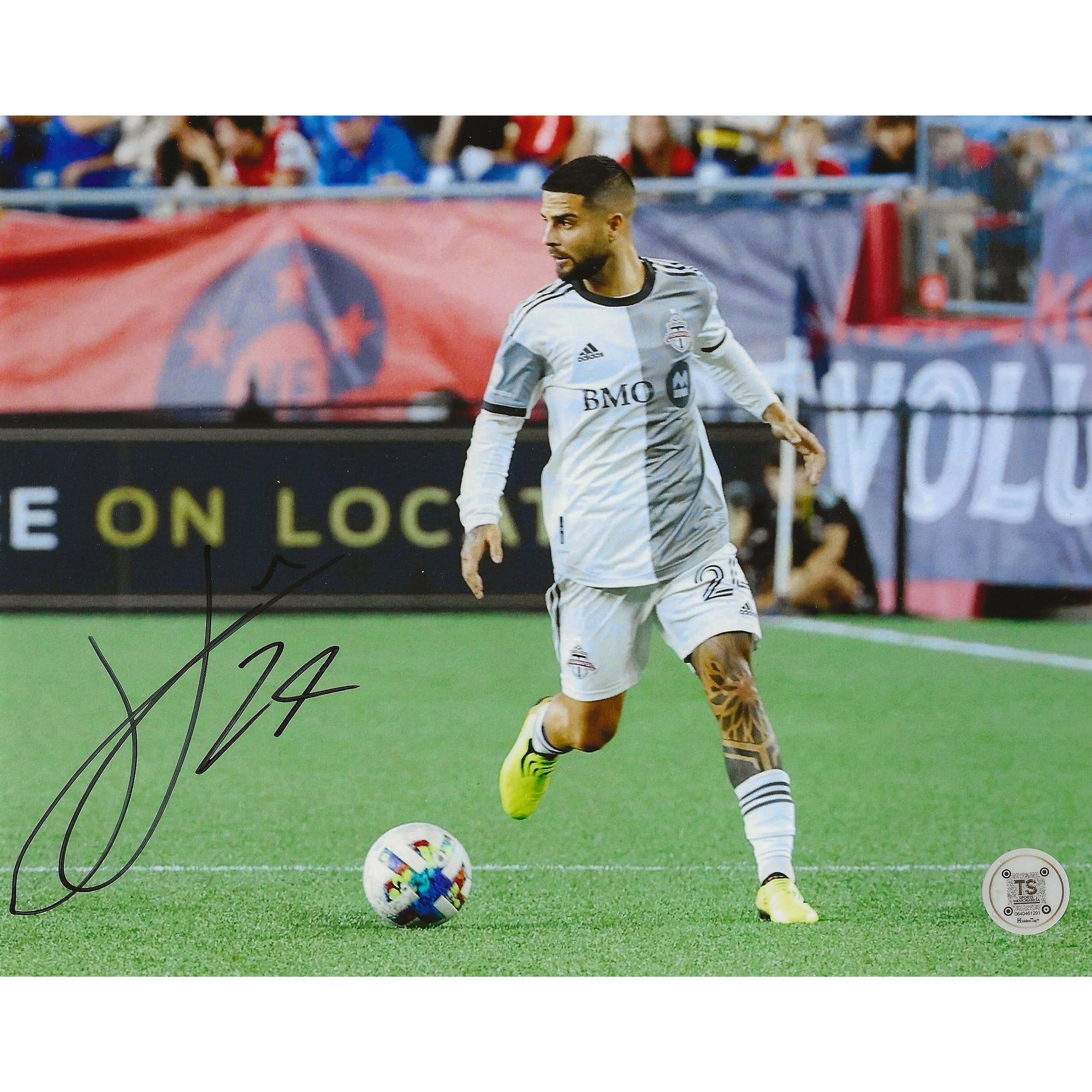 Soccer player in white Toronto FC kit dribbling ball on field with autograph and stadium backdrop