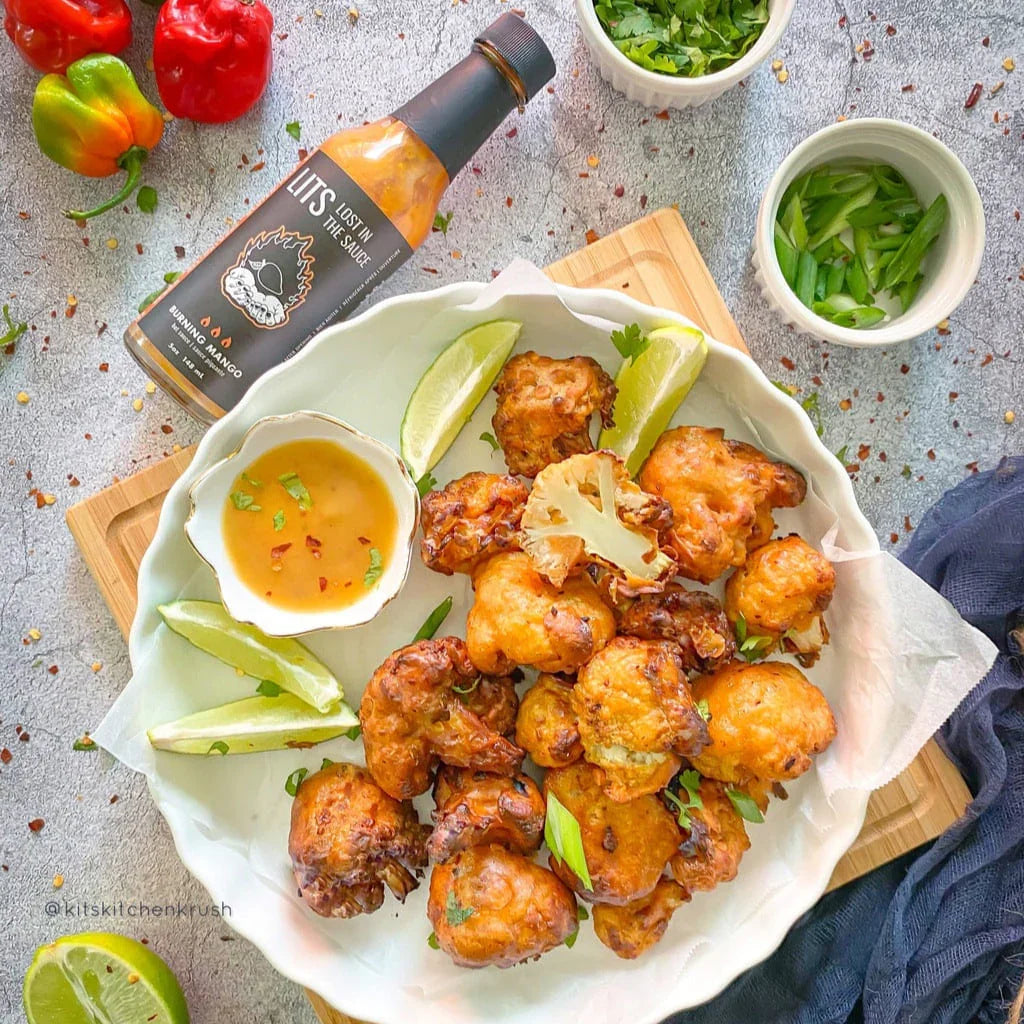 Air fried cauliflower bites with lime, dipping sauce, hot sauce bottle, herbs, and peppers