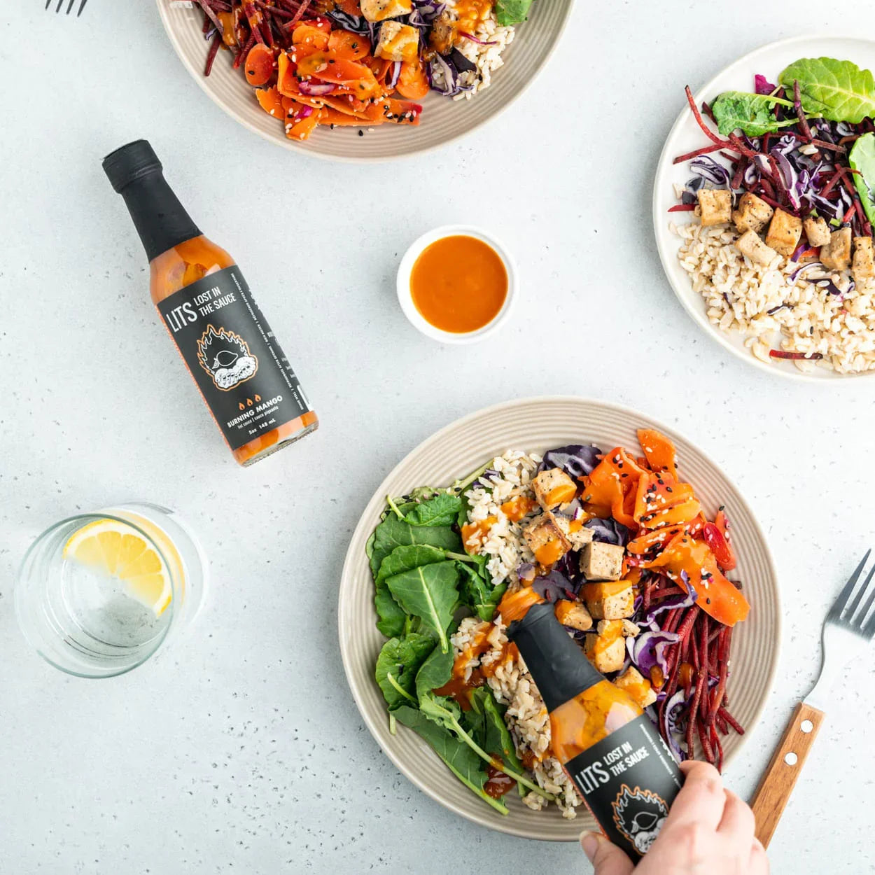Burning Mango hot sauce poured over vegan tempeh salad bowls with rice and fresh greens