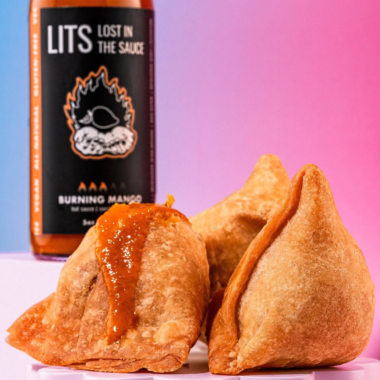 Samosas topped with Burning Mango hot sauce in front of LITS Lost in the Sauce bottle